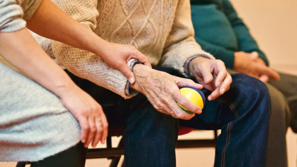 Cuidadora acompañando la mano de un adulto mayor durante una terapia